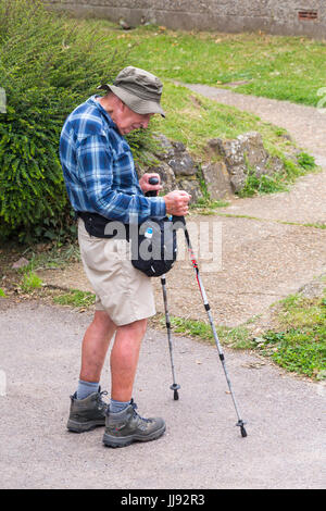 Senior man with walking poles sticks and wearing walking boots to go walking on Isle of Wight, Hampshire, England UK  in July Stock Photo