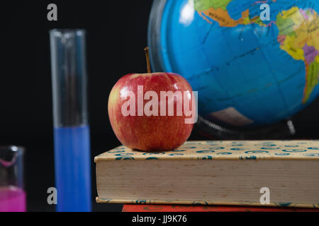 Close-up of globe and books stack with apple on top against black background Stock Photo