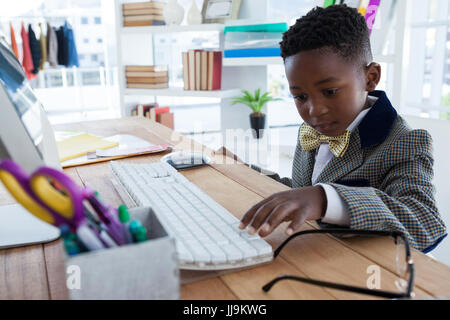 Boy imitating as businessman using computer at desk while working in office Stock Photo