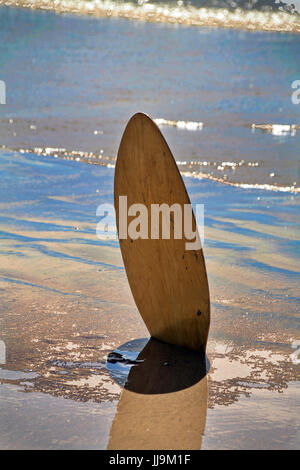 surf board stuck upright in the beach sand next to the sea Stock Photo