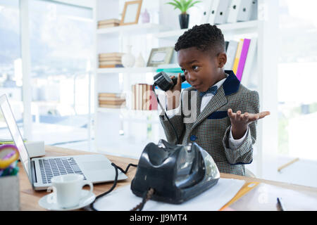 Businessman shrugging while talking on telephone at office desk Stock Photo