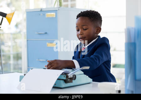 Boy imitating as businessman using typewriter at desk in office Stock Photo
