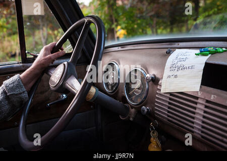 A driver has one hand on the steering wheel of an antique Chevrolet pickup truck with a to-do list on the dashboard. Stock Photo