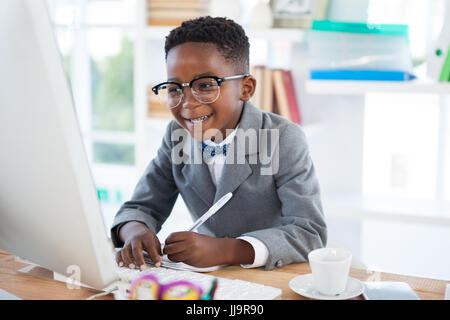 Smiling businessman writing report while looking at laptop in office Stock Photo