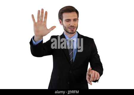 Smiling businessman in suit using invisible interface while standing against white background Stock Photo