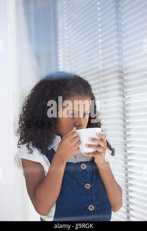 Businesswoman having coffee while standing by window in office Stock Photo