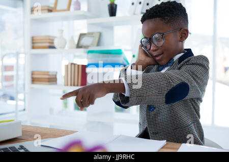 Businessman talking on phone and pointing while sitting at desk in office Stock Photo