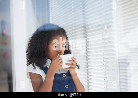 Girl imitating as businesswoman having coffee while standing by window seen through glass Stock Photo