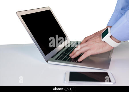 Cropped hand of businessman wearing smart watch while using laptop at table against white background Stock Photo