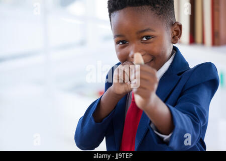 Portrait of boy imitating as businessman playing with rubber band while standing in office Stock Photo