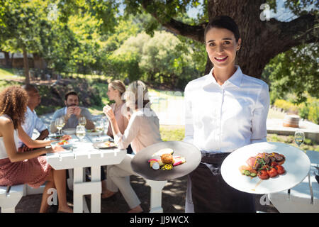 Portrait of smiling waiter holding plates of foods in restaurant Stock Photo