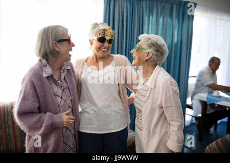 Senior female friends wearing novelty glasses while talking in nursing home Stock Photo