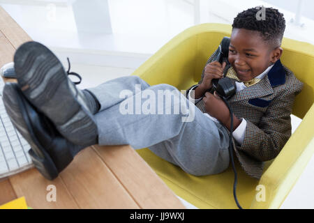 High angle view of happy boy imitating as businessman talking on landline phone while sitting on armchair against white background Stock Photo