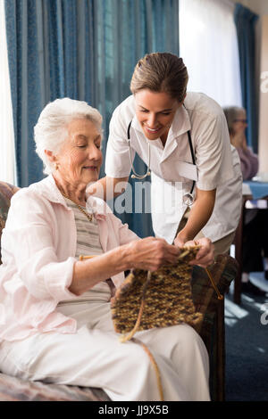 Senior woman showing knitting fabric to female doctor at retirement nursing home Stock Photo