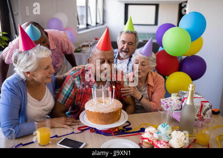 Senior man blowing candles on birthday cake while enjoying with friends at party Stock Photo