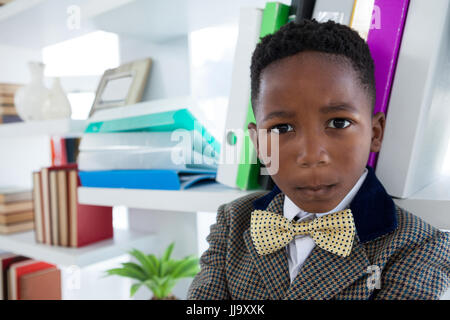 Close up portrait of boy imitating as businessman standing by shelf in office Stock Photo