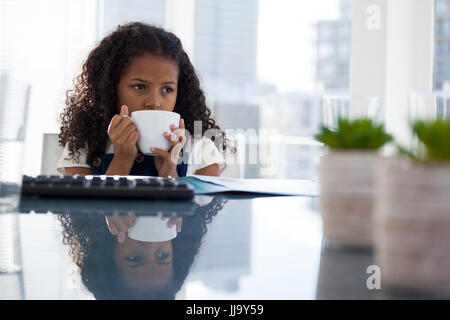 Thoughtful businesswoman having coffee while sitting at desk in office Stock Photo
