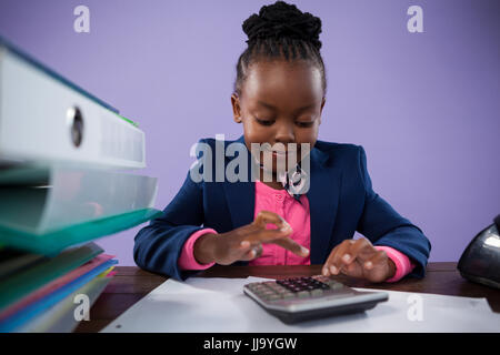 Businesswoman using calculator while doing paperwork at desk against purple wall in office Stock Photo