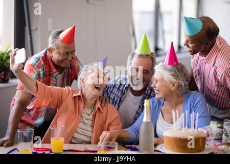 Cheerful senior woman taking selfie with friends through mobile phone at birthday prty Stock Photo