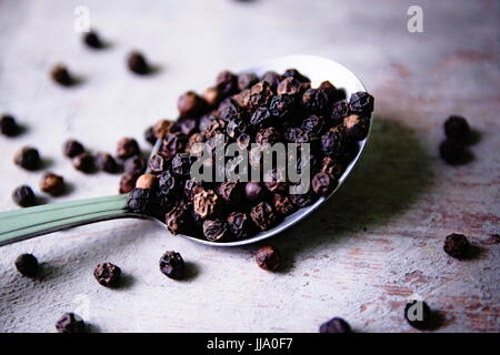 Fresh spicy peppercorns on an antique spoon placed on a wooden background. Stock Photo