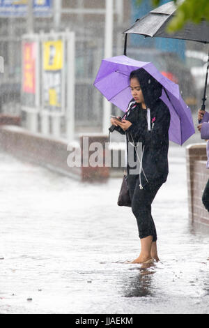 A woman walks through flash flooding water on her way home after heavy rain caused flash flooding to the A525 in summer during thunder and lightning storms that hit the area, Rhyl, North Wales, UK Stock Photo