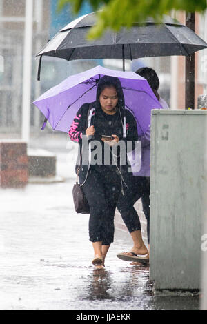 A woman walks through flash flooding water on her way home after heavy rain caused flash flooding to the A525 in summer during thunder and lightning storms that hit the area, Rhyl, North Wales, UK Stock Photo