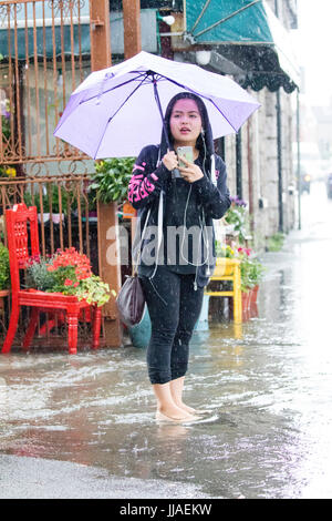 A woman walks through flash flooding water on her way home after heavy rain caused flash flooding to the A525 in summer during thunder and lightning storms that hit the area, Rhyl, North Wales, UK Stock Photo