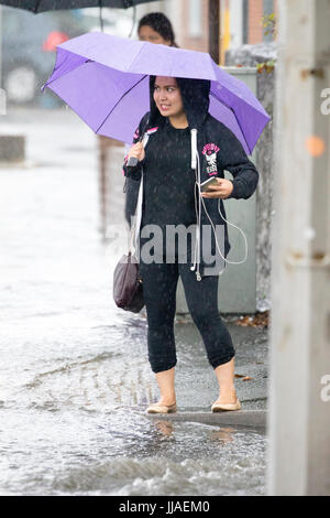 A woman walks through flash flooding water on her way home after heavy rain caused flash flooding to the A525 in summer during thunder and lightning storms that hit the area, Rhyl, North Wales, UK Stock Photo