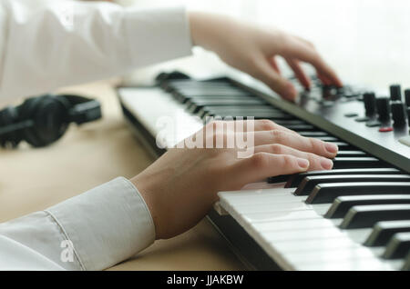 Woman tuned synthesizer, and play on it. Dressed in a white shirt, side view. In the frame are two hands Stock Photo