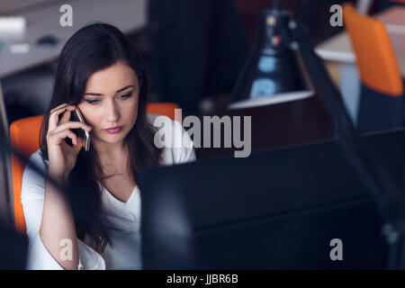 Beautiful young woman working on computer and talking on phone Stock Photo