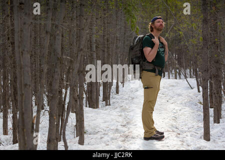 A male hiker pauses in the forest and snow along the Taggart Lake Trail in Jackson Hole. Grand Teton National Park, Wyoming Stock Photo