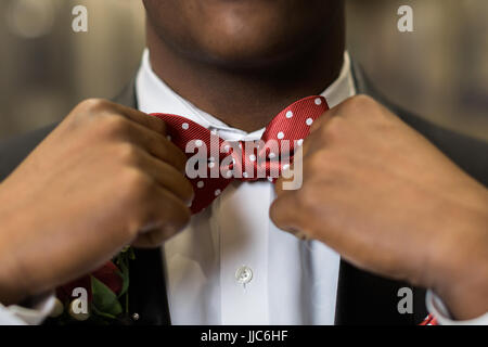 One teen boy adjusts polka dotted red bow tie. Getting dressed and ready for formal high school prom dance. Stock Photo