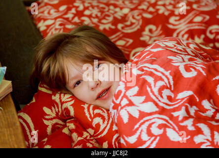 A small diseased girl in the bedroom. Little girl sitting on a bed wearing a pajamas. Stock Photo
