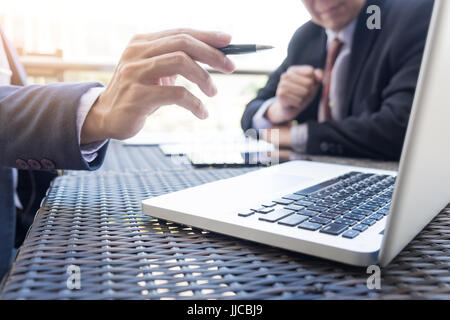 Two businessmen discussing planing tasks with laptop computer sitting at outdoor table. Stock Photo