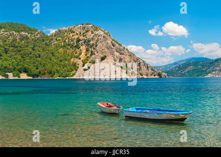 two small boats tied with rope at Aegean sea bay with turquoise waters surrounded by mountains on sunny day, Marmaris, Turkey Stock Photo