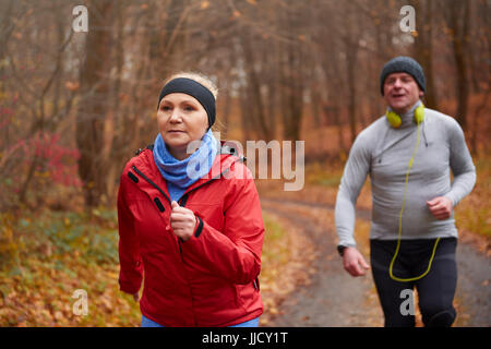 Mature couple running through forest path Stock Photo