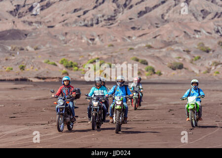 Group of off road motor bikers ride across the ash flats of Mt Bromo, Java, Indonesia. Stock Photo
