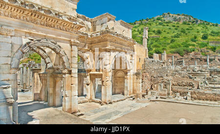 panoramic view of ancient greek buildings near Celsus Library in Ephesus on sunny day with green hill and blue sky in background, Turkey Stock Photo