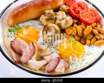 English breakfast with fried egg, beans, tomatoes, mushrooms, bacon and sausage on white plate Stock Photo