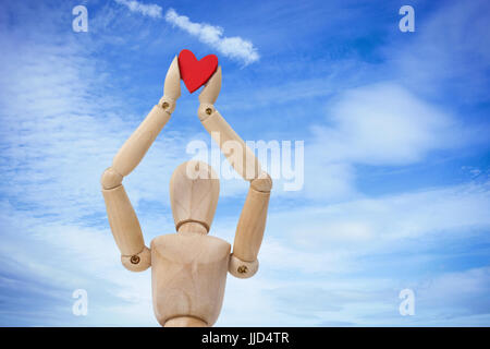 Wooden three dimensional figurine holdingred heart on top against low angle view of cloudy sky Stock Photo