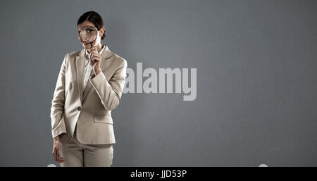 Businesswoman looking through magnifying glass against grey background Stock Photo