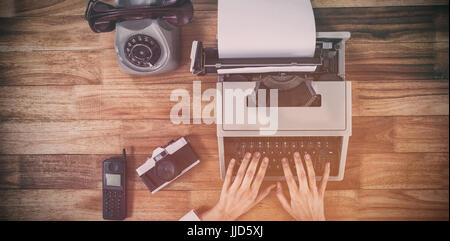 Overhead view of businesswoman typing on typewriter by vintage camera and phone Stock Photo