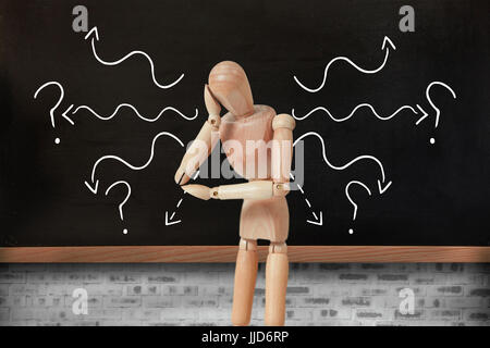 3d Thoughtful wooden figurine pretending to lean  against blackboard on wall Stock Photo