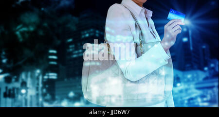 Mid section of woman holding credit card against illuminated roads by building in city Stock Photo