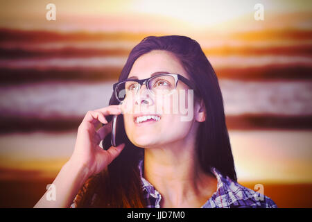 Close up of young woman talking on phone against image of a sunset over the waves Stock Photo