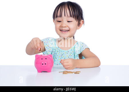 Asian Chinese little girl putting coins into piggy bank in isolated white background Stock Photo