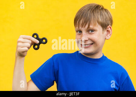 Young beautiful happy boy with freckles blue t-shirt holding fidget spinner on yellow background. Stock Photo