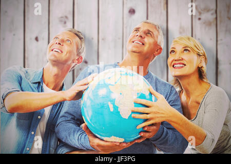 Smiling people looking up while holding globe against wooden planks Stock Photo
