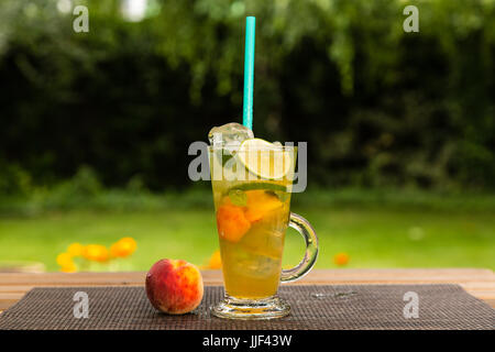 Homemade peach ice green tea with lime and lemon balm. On a wooden table outdoors in the garden. Healthy beverages concept. Stock Photo