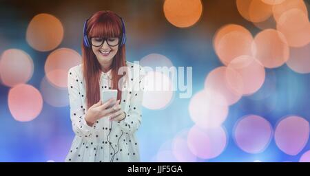 Digital composite of Smiling beautiful woman listening music through headphones while standing against defocused lights Stock Photo